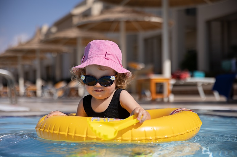 Cute little girl in a hat and sunglasses plays in the pool while sitting in a swimming circle.