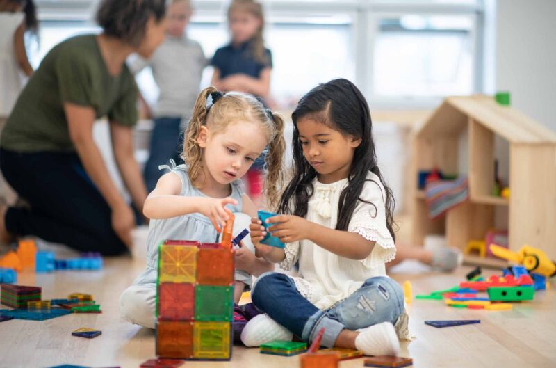 Two preschool girls are working together to build using magnetic tiles.