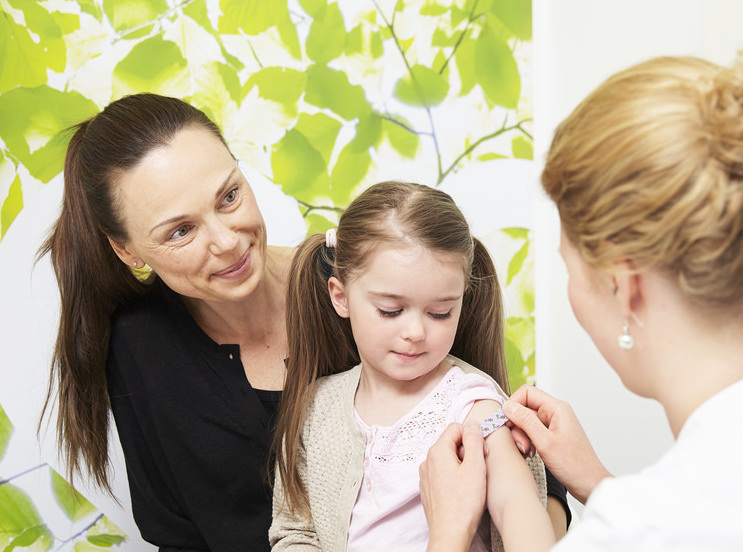 Doctor/nurse giving girl a vaccination with mother
