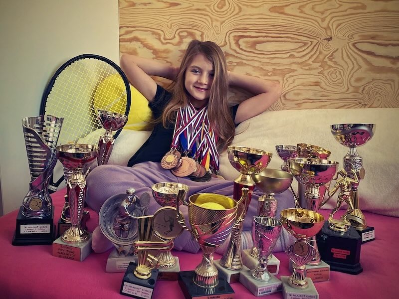 Girl sitting in bed with lots of medals and trophies