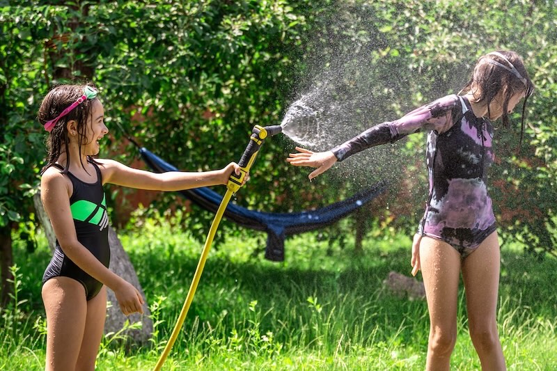 Adorable little girls playing with a garden hose on hot summer day. Children having fun with water, outdoor summer activities for kids.