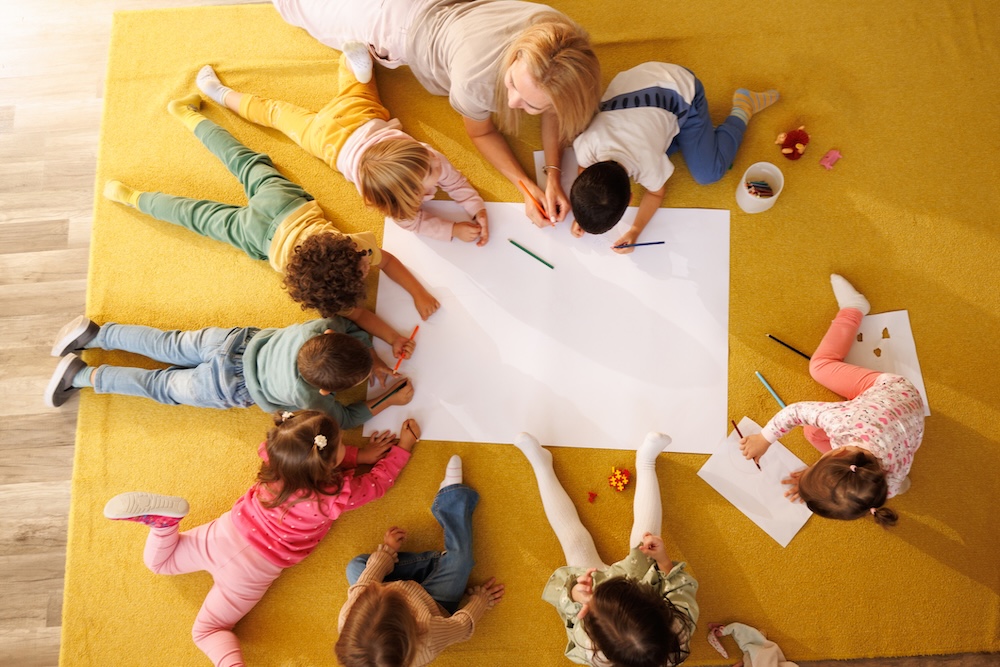 Teacher and little children drawing on big white paper together